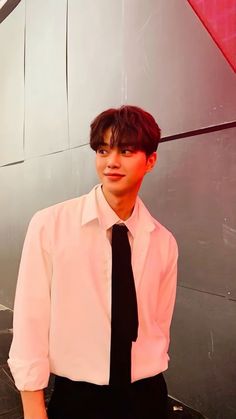 a young man wearing a white shirt and black tie standing in front of a wall