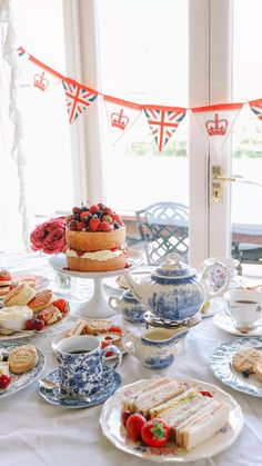 a table topped with cakes and desserts next to a window covered in bunting