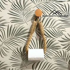 a toilet paper roll hanging from a rope on a palm leaf wallpapered bathroom