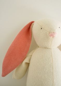 a white stuffed animal with an orange nose and ears, sitting against a white wall