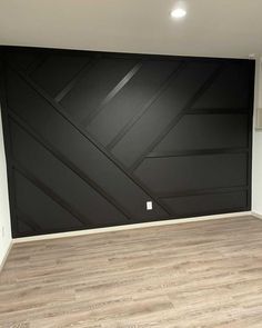 an empty room with wood flooring and black painted wall behind the door is a white light