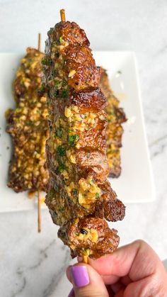 someone holding up a skewer of food on a white plate with other items in the background