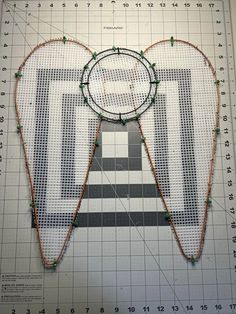 a piece of art made out of string and beads on a table with a ruler next to it