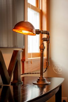 an old fashioned desk lamp sitting on top of a wooden table next to a window