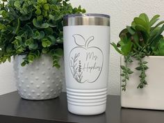 a white tumbler sitting on top of a table next to a potted plant