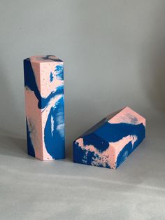 two blue and pink painted blocks on a white surface with one block leaning up against the other