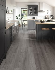 a large kitchen with gray cabinets and wood flooring is pictured in this image, there are two stools on the counter