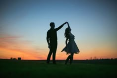 a man and woman dancing in the grass at sunset