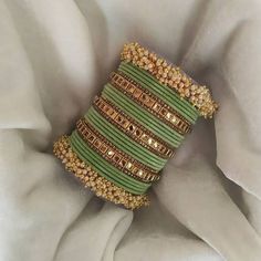 a green and gold bracelet on top of a white cloth