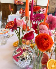 the table is set with oranges, pink and red flowers and candles in vases