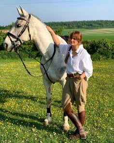 a woman standing next to a white horse on a lush green field