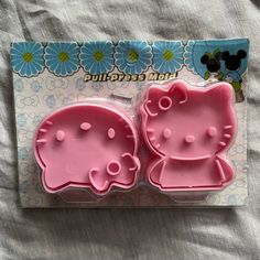 two pink hello kitty cookie cutters sitting on top of a bed