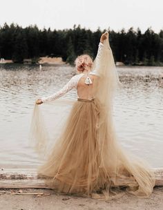 a woman in a long dress standing on the beach with her back to the camera