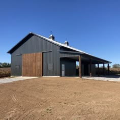 an empty barn sits in the middle of a dirt field with a fence around it