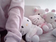 a person in pink is holding several stuffed animals on a bed with white sheets and pillows