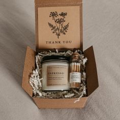 an open gift box containing two candles and a thank you card in the bottom right corner