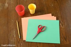 a pair of red scissors sitting on top of a piece of paper next to some cups