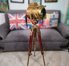 an old fashioned camera on a tripod in front of a grey couch with pillows