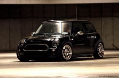 a small black car parked in a parking garage next to a wall and cement floor