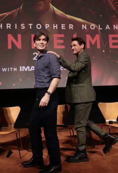 two men standing next to each other in front of a large screen with the movie poster behind them