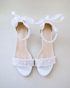 a pair of white shoes with pearls and bows on the toes, tied together by a ribbon