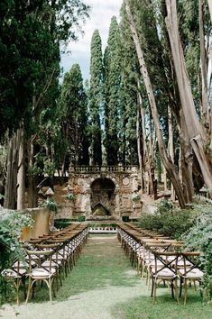 an outdoor ceremony set up with wooden chairs and tables in the middle of trees, surrounded by greenery