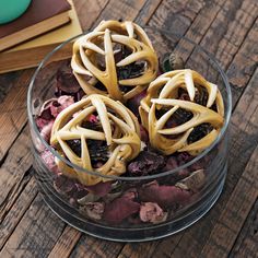 three cookies are in a glass bowl on a table next to books and a cup of coffee