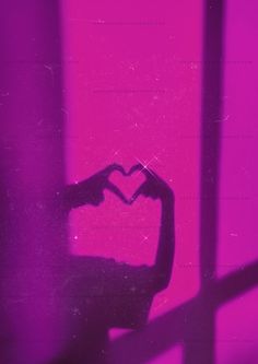 a person making a heart shape with their hands in front of a pink wall and window