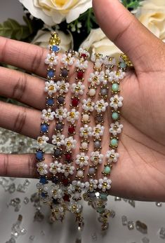 a hand is holding several bracelets with flowers on them and beads in the middle