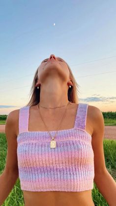 a woman wearing a pink and white crop top in the grass with her eyes closed