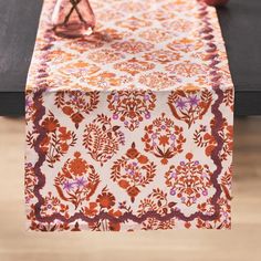 an orange and pink table runner on top of a wooden table with two vases