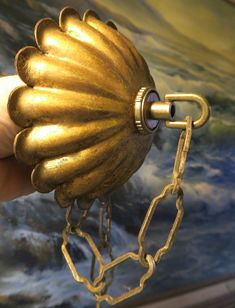 a hand is holding a golden object in front of a painting with chains on it