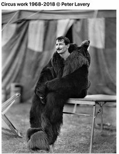 a man sitting on top of a chair next to a big furry bear in front of him