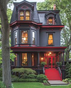 a red and black house with stairs leading up to the front door, surrounded by trees