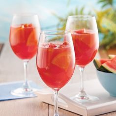 three wine glasses filled with watermelon and orange juice on a table next to a bowl of watermelon slices