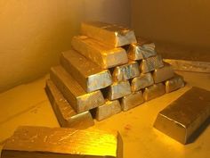 stacks of gold bars sitting on top of a table next to a wall with lights