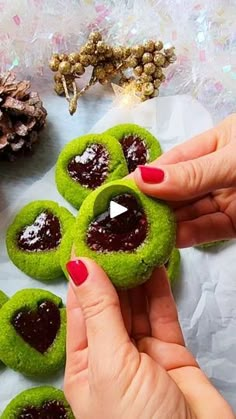 a woman is holding some green cookies with hearts on them and jam in the middle