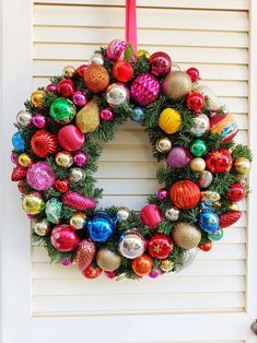 a christmas wreath hanging on the side of a door with ornaments around it and a red ribbon