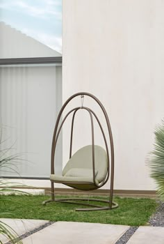 a swing chair sitting in the grass next to a wall and potted planter