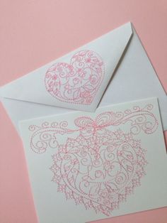 two white envelopes with pink designs on the front and back, one has a heart in it