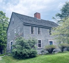 an old gray house sitting on top of a lush green field