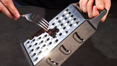 a person holding a fork and knife over a metal grater