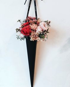 a black vase with flowers hanging from it's side on a wall next to a pair of scissors