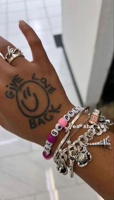 a person's hand with several bracelets and rings on it, including an i love you sign