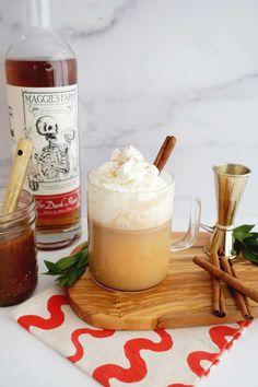 an iced drink with whipped cream and cinnamon sticks on a cutting board next to two bottles of booze