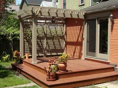 a wooden deck with potted plants on it and a pergolated gazebo in the background