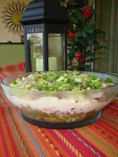 a salad in a glass bowl sitting on top of a colorful table cloth next to a potted plant