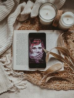 an open book sitting on top of a blanket next to candles and some plants with one person's face on it