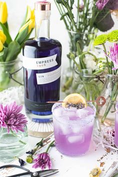 a bottle of blue liquid sitting next to two glasses filled with ice and lavender flowers