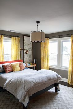 a bedroom with yellow drapes and curtains on the window sill, bed in foreground